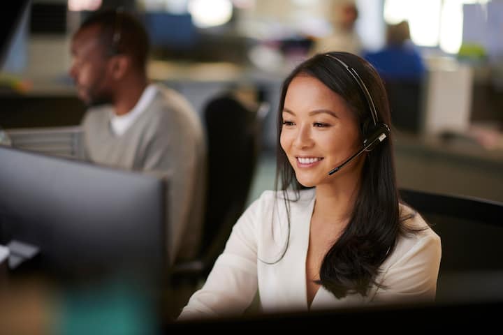 Two people working at desks in an office, wearing headsets and looking at computer screens.