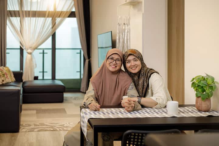 Two people sitting at a dining table in a well-lit apartment with a balcony view in the background.
