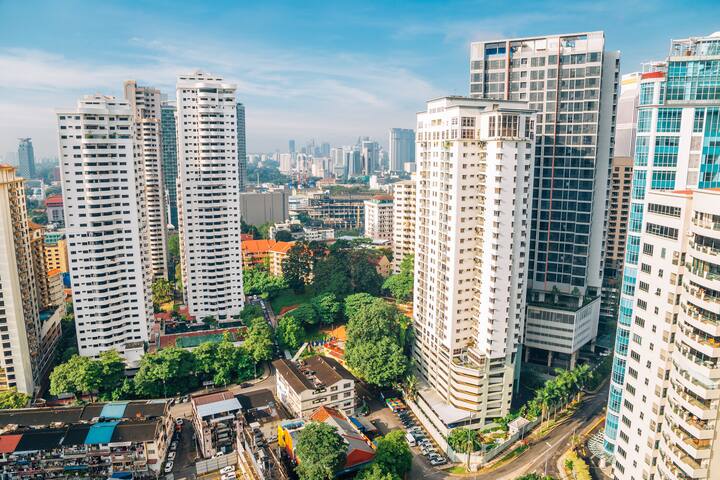 Cityscape view of tall residential buildings with green spaces and smaller structures in the foreground.