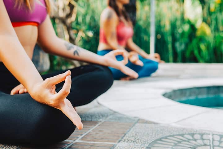 Close-up of individuals in yoga poses by a pool, highlighting hand positions and relaxed ambiance.