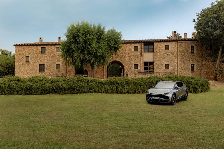 Fachada de una casa rural de piedra en España con un coche negro CUPRA aparcado en el césped, parte de la campaña de escapadas familiares de Airbnb y CUPRA.