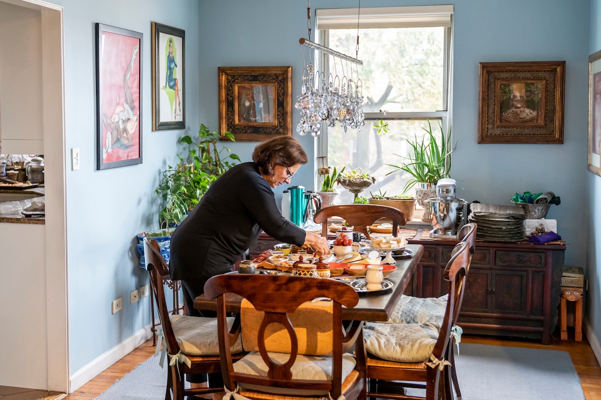 A well-decorated dining area with a person arranging a variety of holiday items on the table, featuring art and plants.