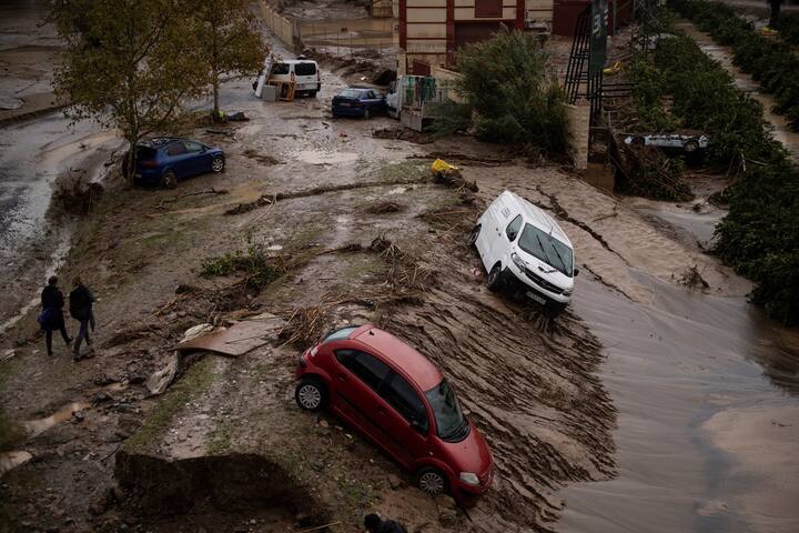 A red car and white van point down a steeply banked mudslide. Other cars sit askew. The light is overcast.