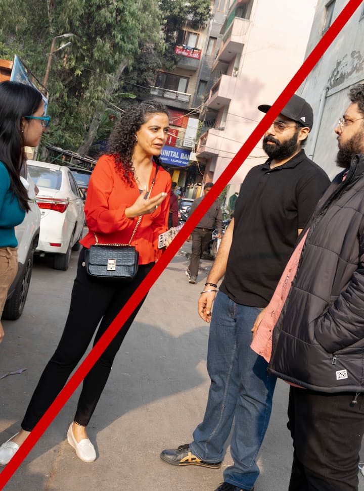 Two groups of people having conversations on a city street, one group includes a person gesturing while talking. Image is tilted.