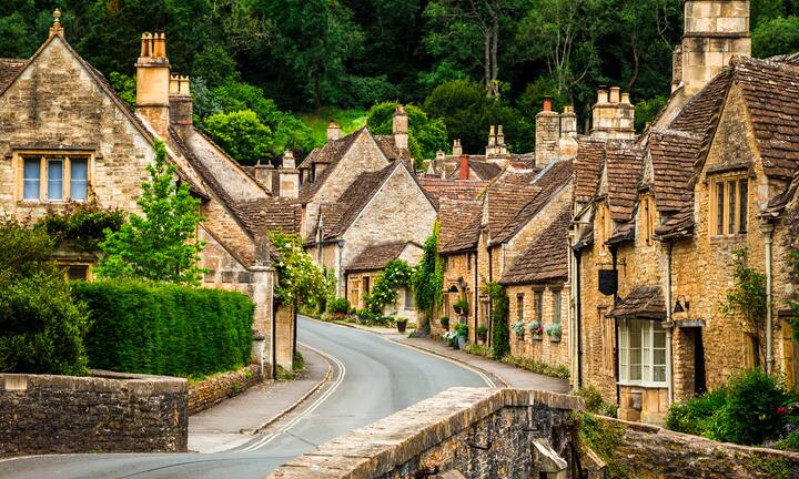 A picturesque village in England with stone houses, a winding road, and lush greenery.