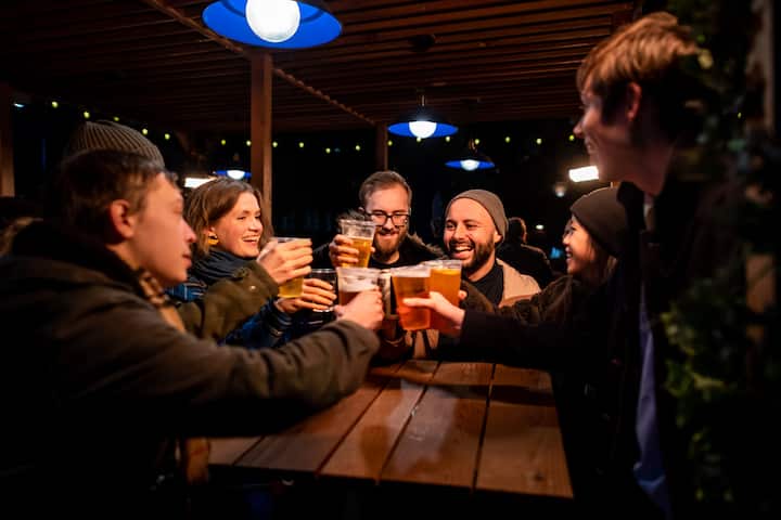 A group of people raising beer glasses in a cosy pub with warm lighting and wooden décor.