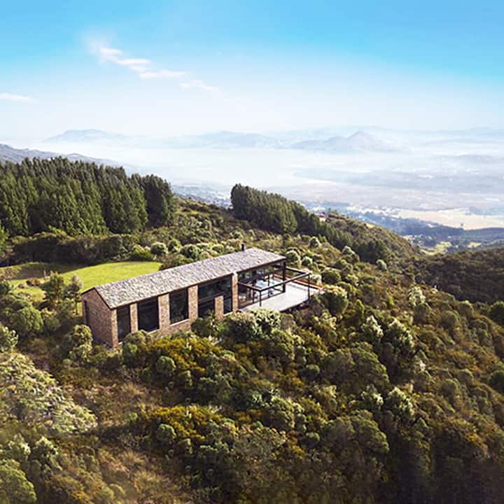 A modern house situated on a green hillside overlooking a valley in Latin America.