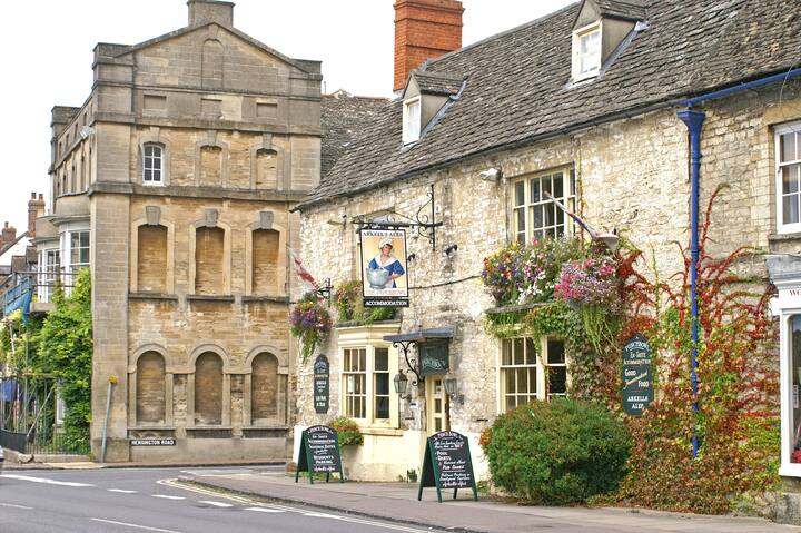 A charming stone pub in England with a sign showing a bird, adorned with hanging flower baskets and greenery along the facade.