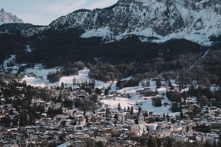 Eine Winterlandschaft mit einer Stadt mit schneebedeckten Gebäuden, umgeben von Bergen und immergrünen Bäumen.