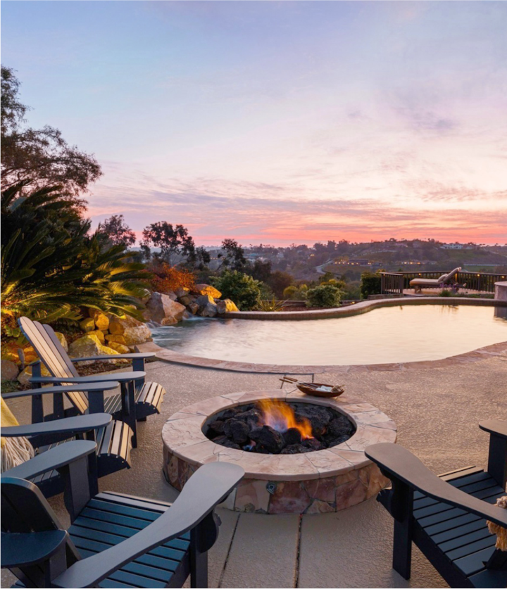 Duas cadeiras estão perto de uma fogueira, com vista para uma piscina que reflete a luz do sol poente.