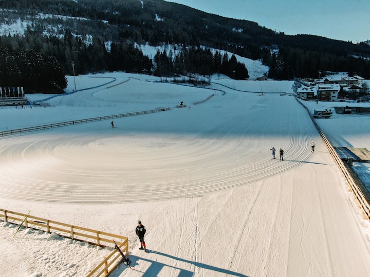 A snow-covered ski resort with skiers on a sunny day, surrounded by forested mountains.