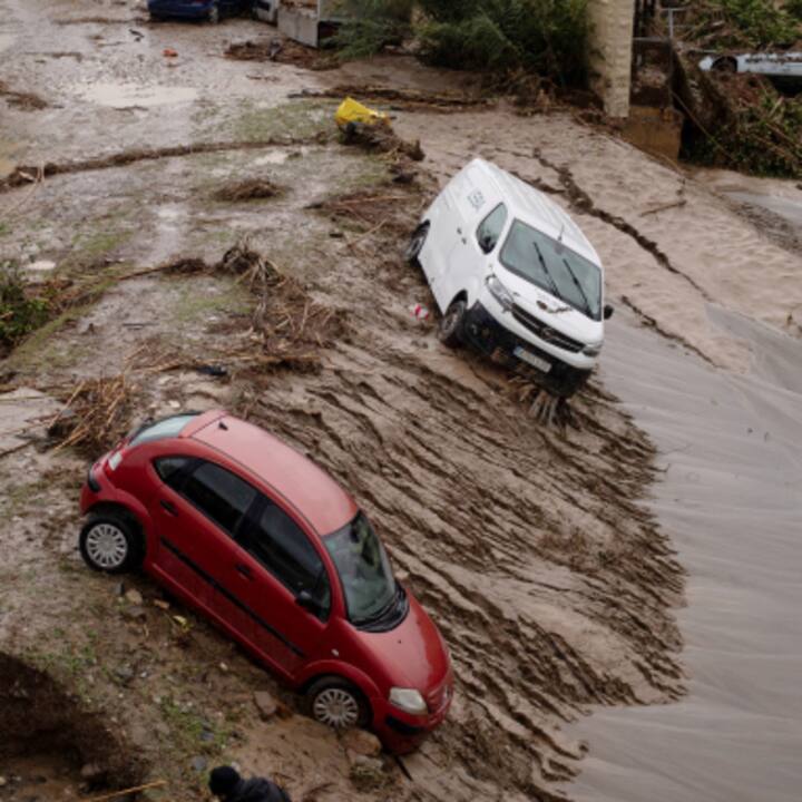 Flood-damaged red car and white van leaning on muddy ground after a crisis.