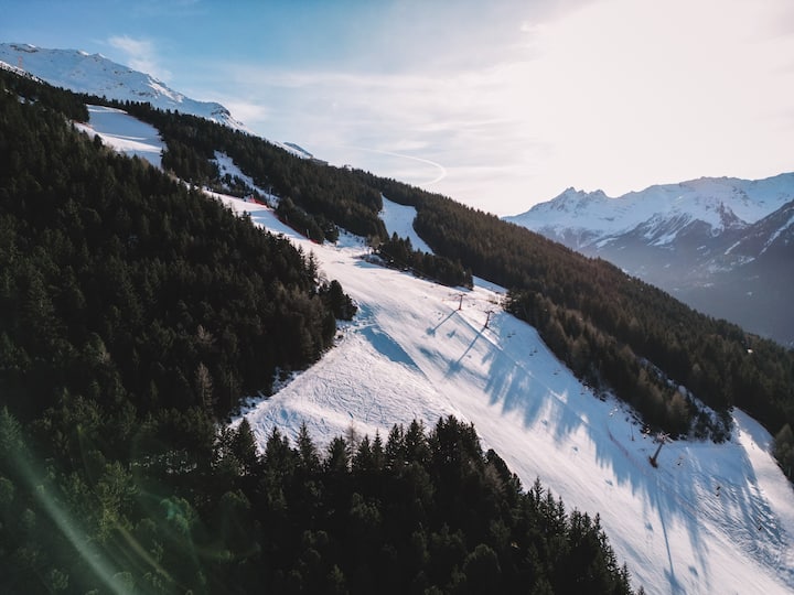 Eine schneebedeckte Berglandschaft mit Skipisten, die von dichten Wäldern umgeben sind – wahrscheinlich eine Stadt, in der Veranstaltungen stattfinden.
