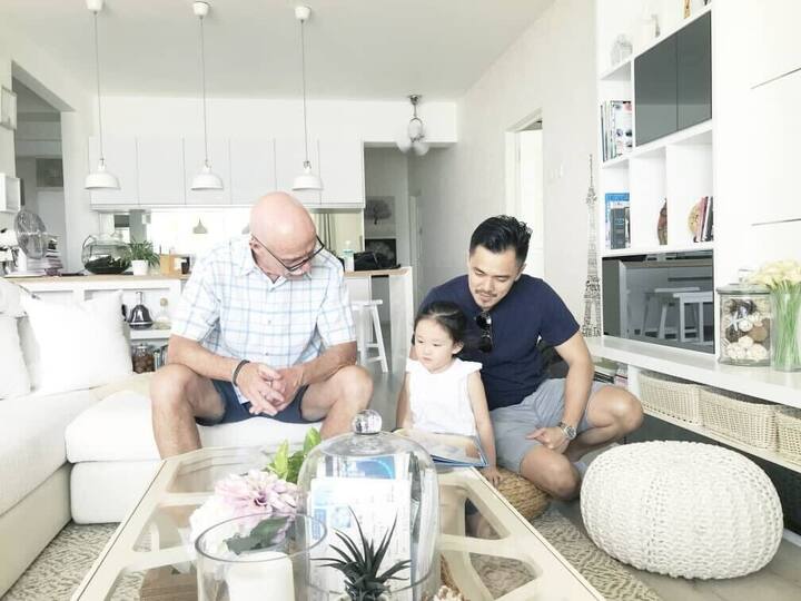Two adults and a child sitting together in a bright, modern living room with a white interior and decorative plants.