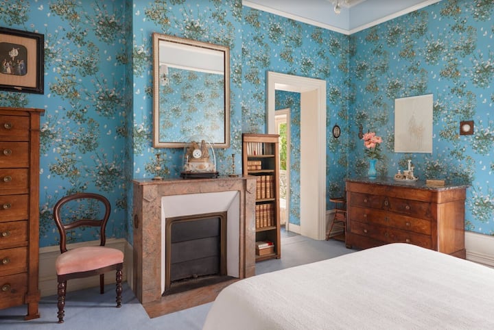 Elegant bedroom with blue floral wallpaper, antique furniture, and a marble fireplace.