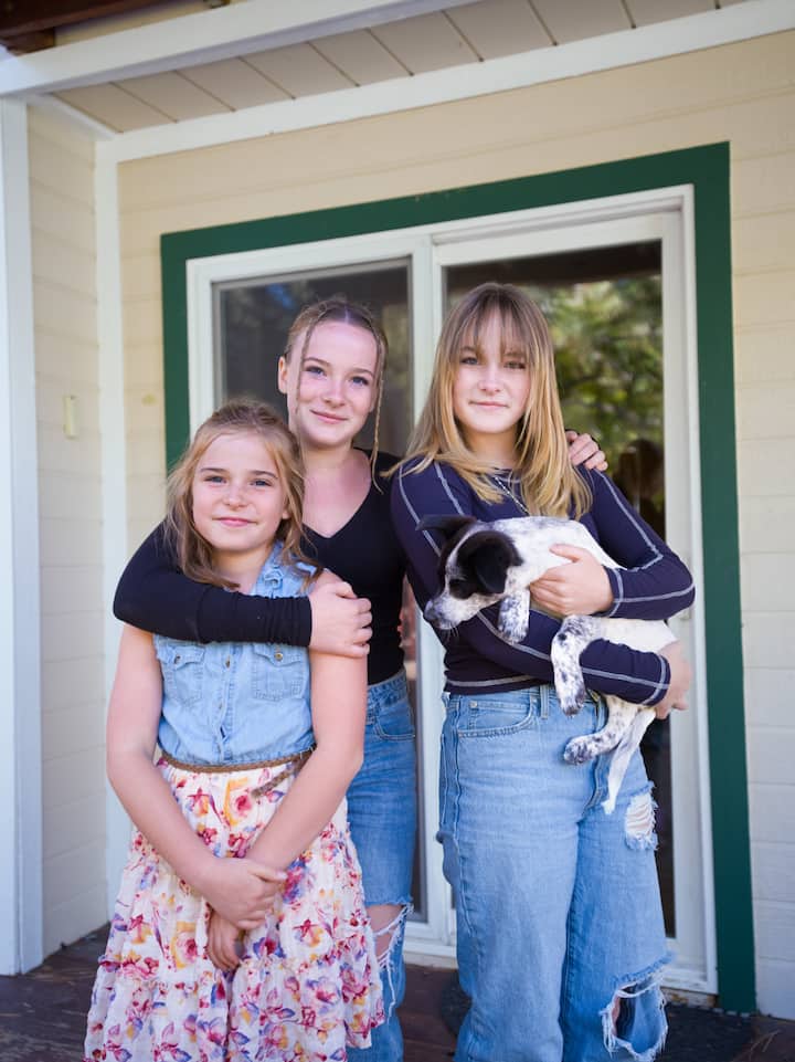 Three girls stand together, with the one on the right holding a dog. 
