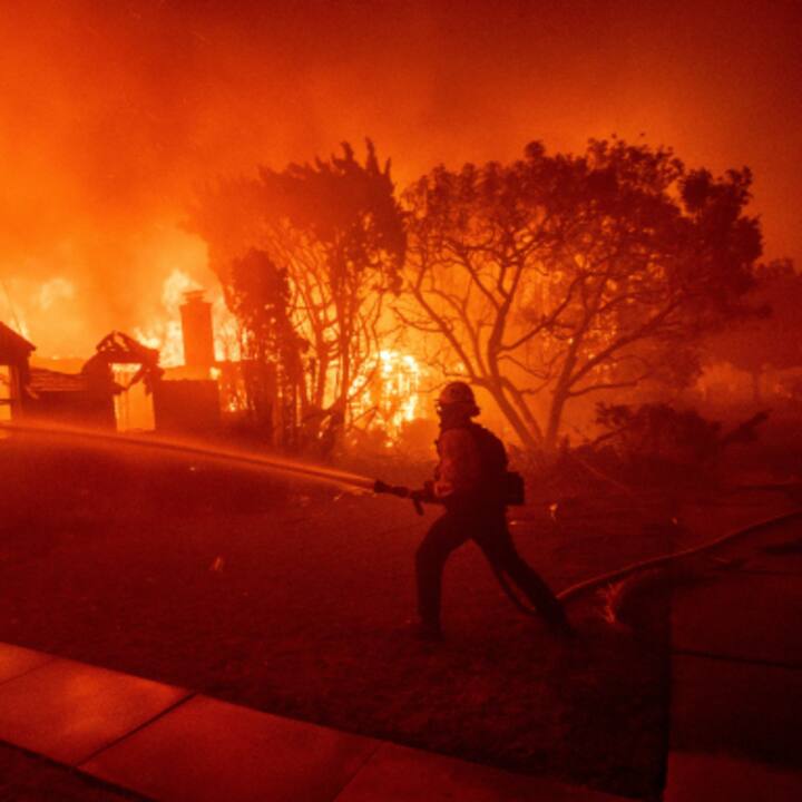 Firefighter battling a large, intense wildfire engulfing homes and trees in Los Angeles at night.