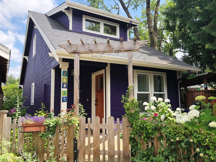 Charming purple house with white trim, small garden, and wooden picket fence.