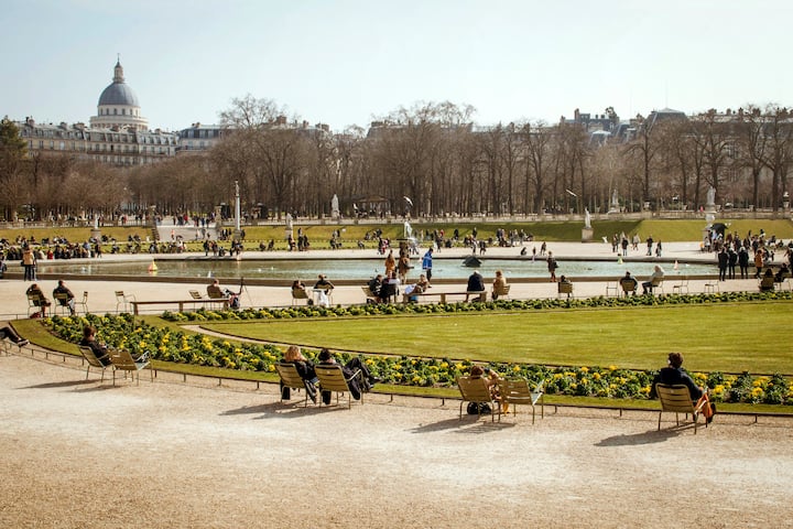 Luxembourg Gardens, Paris, with people sitting on benches, strolling around a pond, and the Pantheon dome in the distance.