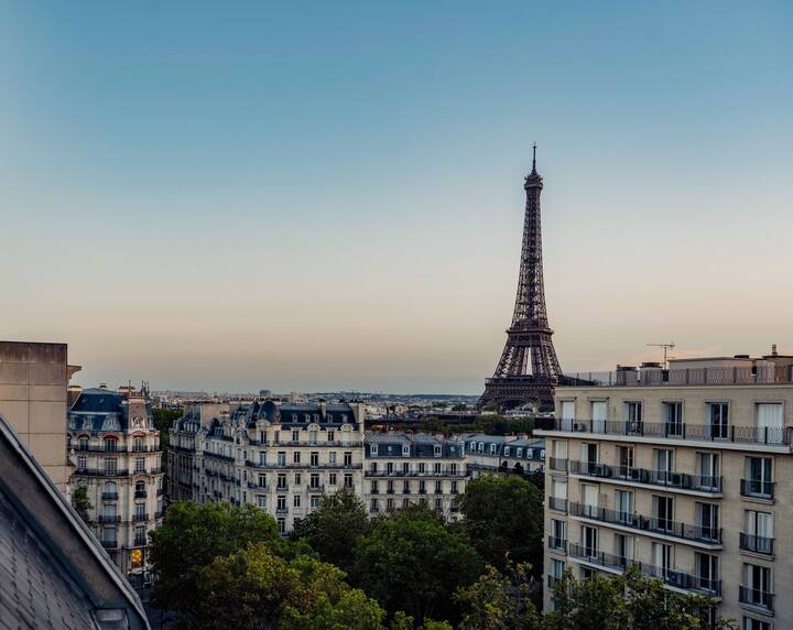 Paris cityscape featuring the Eiffel Tower during sunset, with surrounding buildings and trees.