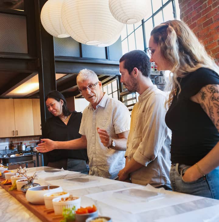 A group of people participating in a cooking class, with various ingredients and kitchen tools laid out on the table.