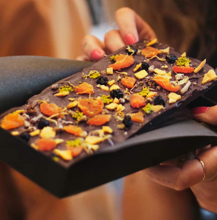 Close-up of a dark chocolate bar with various toppings including dried apricots, nuts, and berries