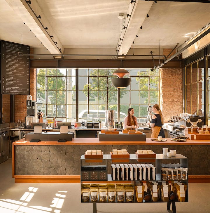 Interior of a bright, spacious coffee shop with two women talking behind the counter and various coffee products displayed in the foreground.
