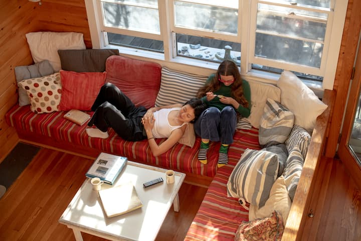 Two people sit on an el couch near a window in a room with wooden interior.