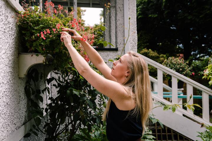 Woman reaches up to adjust flowers in plant box under window