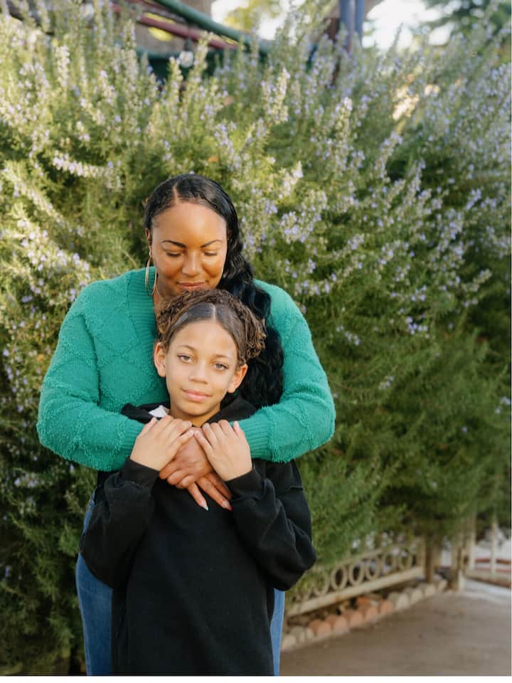 緑色のセーターを着た母親が、黒いスウェットシャツを着た息子を抱きしめて立っています