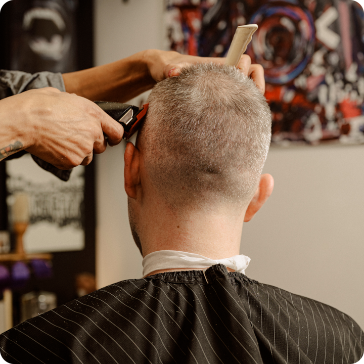 Close-up of a barber using clippers and a comb to trim a man's short hair.