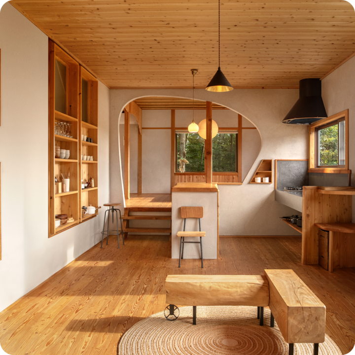 Interior of a cozy, rustic room with wooden furniture, shelves, and a kitchen area, emphasizing a welcoming and serene atmosphere.