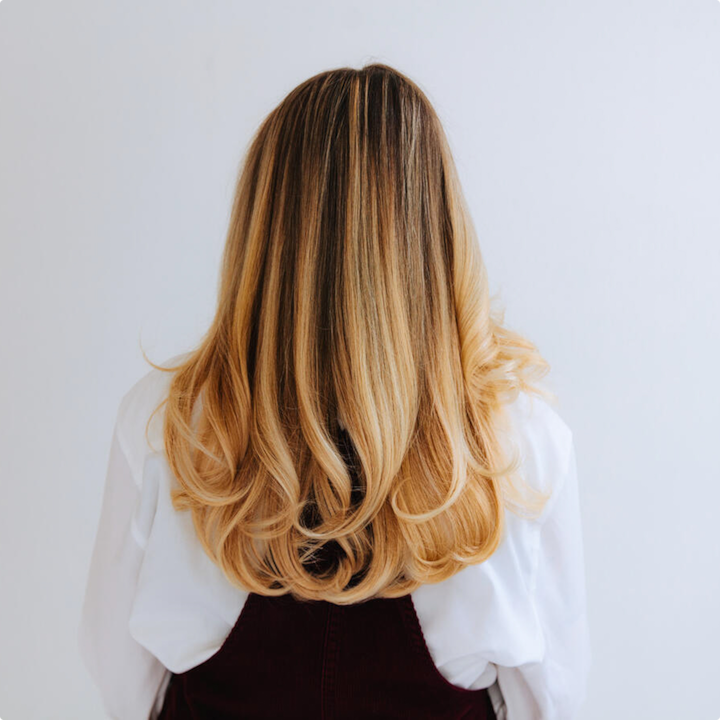 Back view of a woman with long, perfectly styled blonde hair cascading down her back, showcasing a beauty offering.