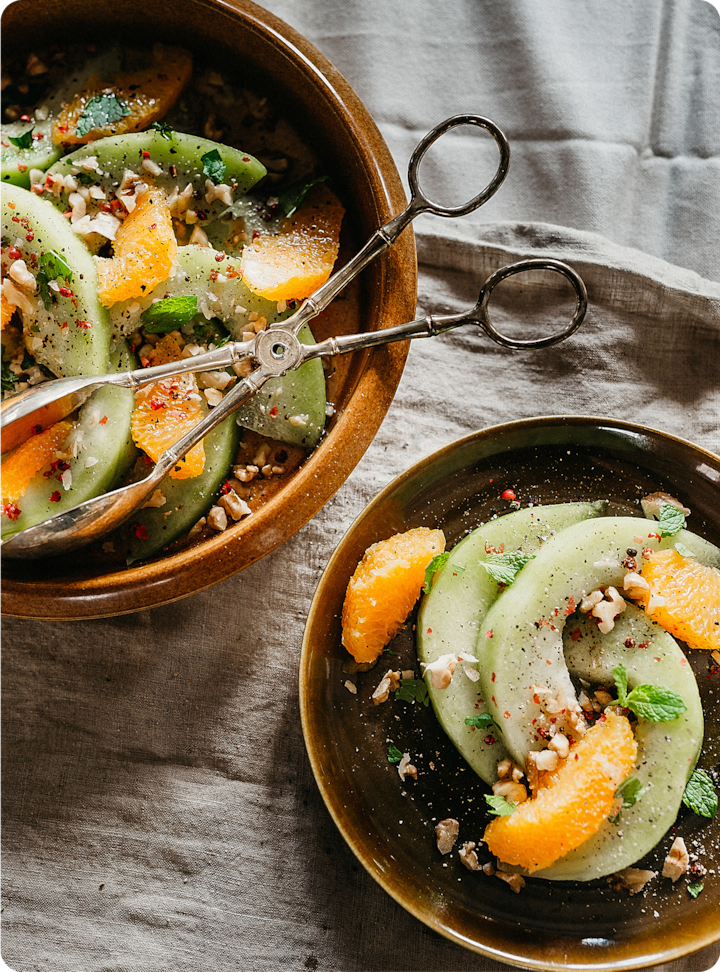 Rustic table setting showing fresh salad with orange slices, mint leaves, and chopped nuts in two bowls, complemented by vintage scissors.