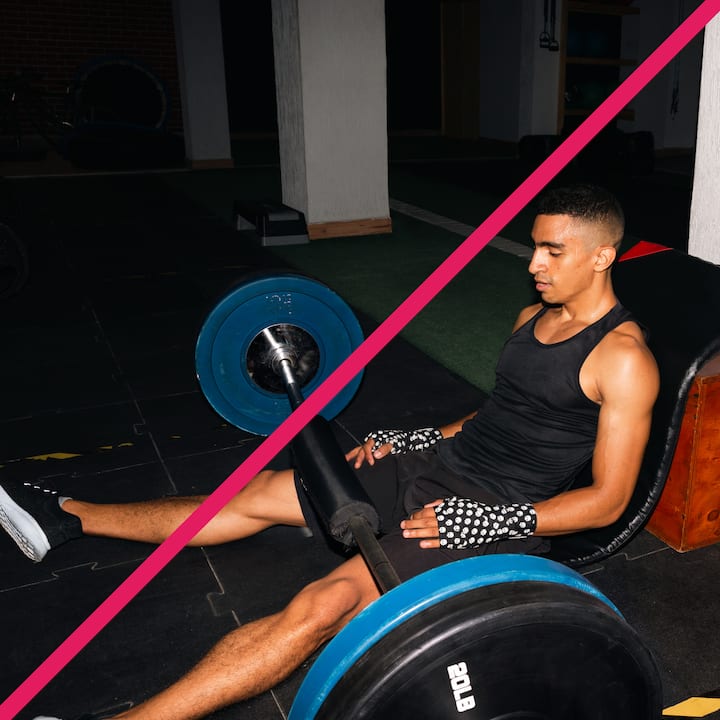 A person in gym attire sitting on a bench near a barbell, the gym is dimly lit with minimal background distractions.