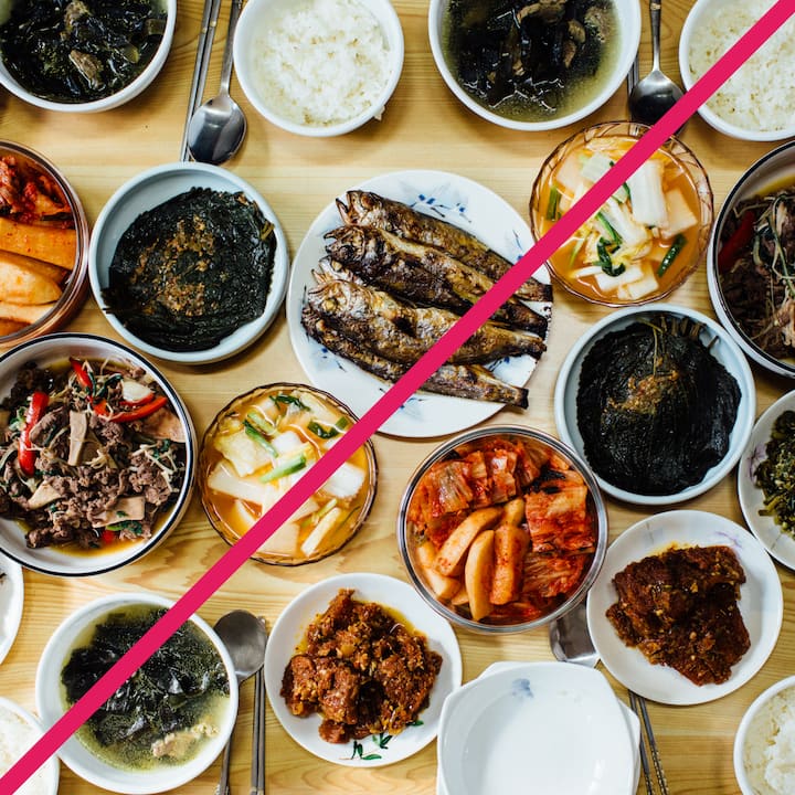 A top-down view of a table filled with various Korean dishes, including grilled fish, kimchi, and soups, divided diagonally by a pink line.