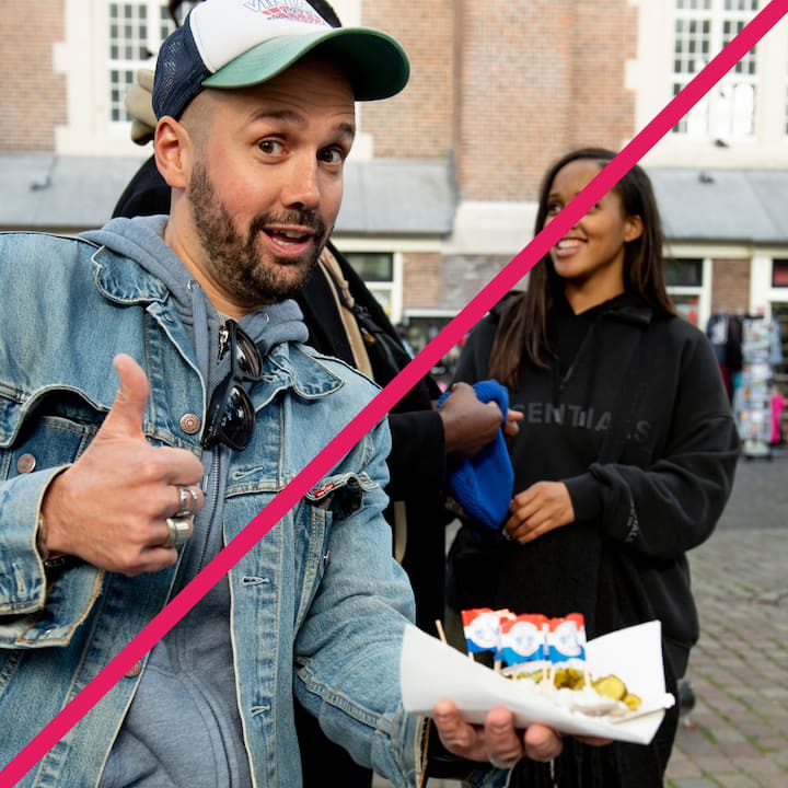 Man in denim jacket giving thumbs up and holding food in a cone, standing in front of a building with a group of people.