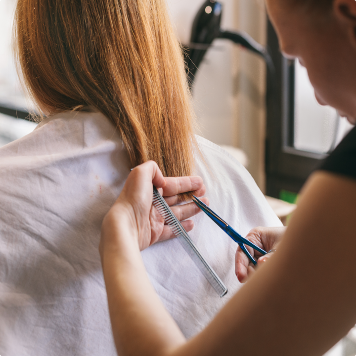Close-up of a stylist cutting brown hair with scissors and a comb.