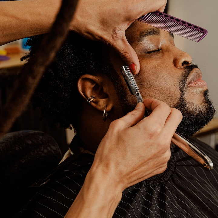 Un barbier qui taille soigneusement la barbe d'un client, mettant en avant des services de soins professionnels.