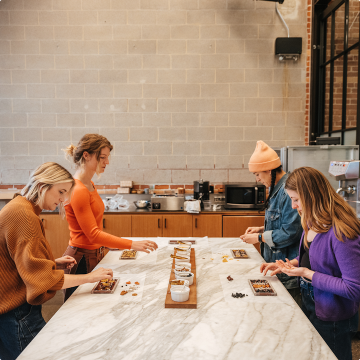 Quatre personnes sont debout autour d'une table en marbre. Elles posent des aliments dans de petits plateaux dans une cuisine.