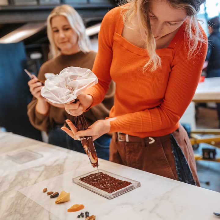 Une personne qui porte un pull orange verse du chocolat dans un moule lors d'une expérience.