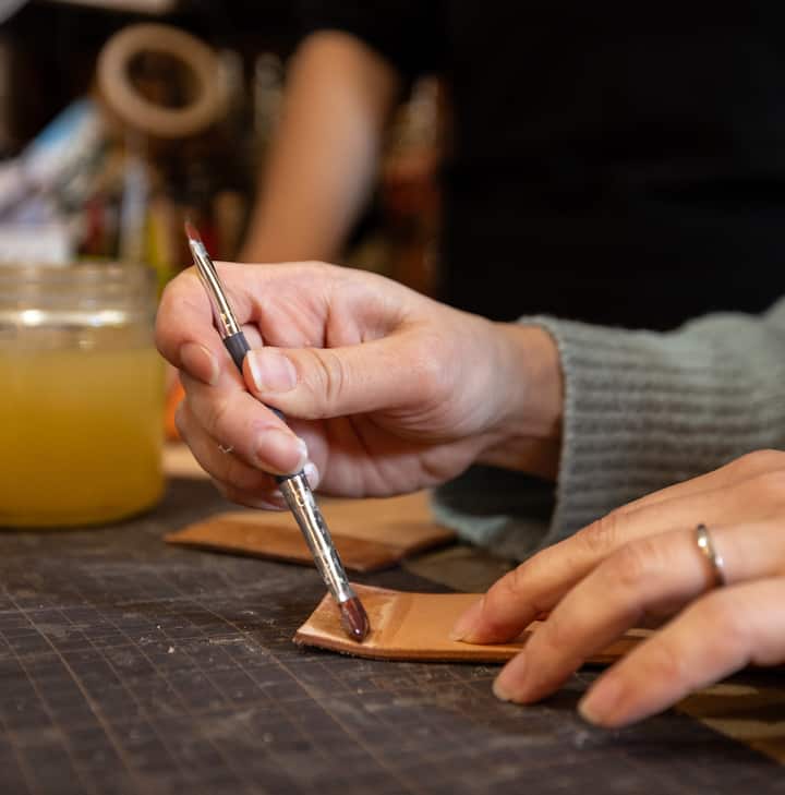 Close-up of a person painting a piece of leather with a small brush.