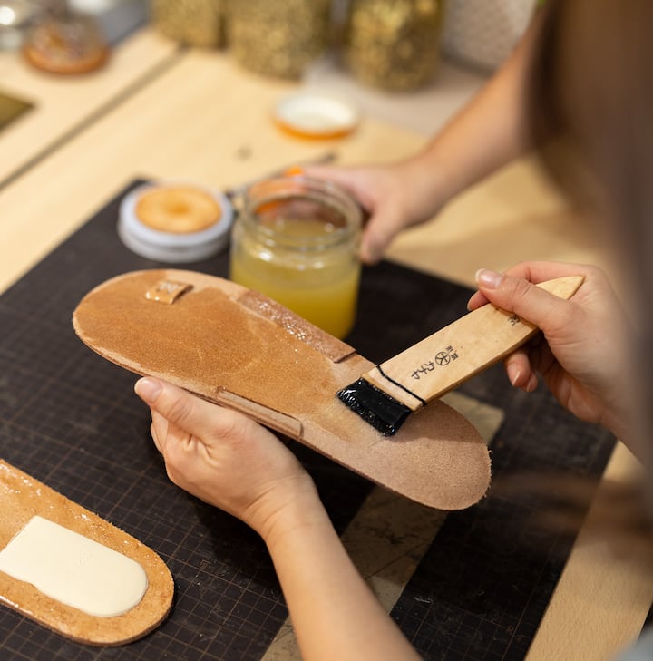 Person applying glue to the sole of a handmade shoe with a brush.
