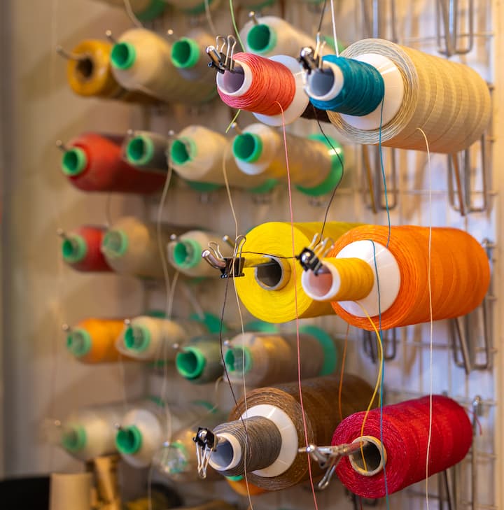 Colorful spools of thread in various shades, including red, yellow, blue, and green, neatly arranged on a wall-mounted rack.