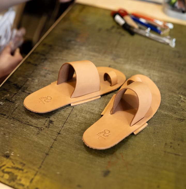 Handcrafted leather sandals on a workbench with tools in the background.