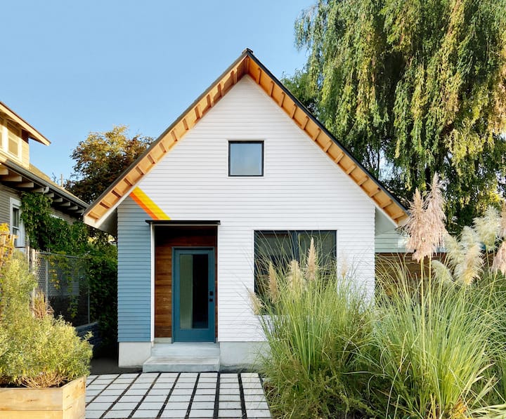 A modern house with a gabled roof and a bold blue front door surrounded by a tree and green landscaping.