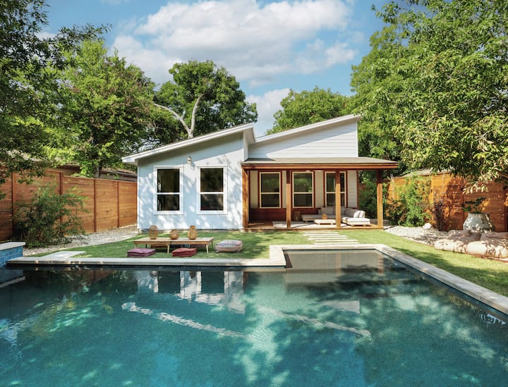 Ağaclarla əhatə olunmuş hovuzu və taxta hasarı olan müasir evin günəşli arxa həyəti. 