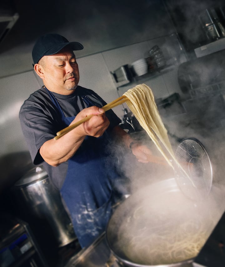 A chef strains freshly-cooked ramen noodles in a restaurant kitchen.