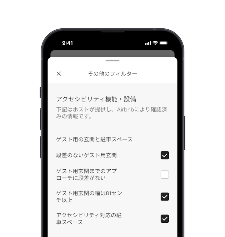 スマートフォンの画面に、多くの検索フィルターのひとつであるその他の絞り込みが、画面上の重なったパネルに表示されています。「アクセシビリティ機能・設備」という見出しのセクションがあります。その下には、アクセシビリティ機能・設備が「ゲスト用玄関と駐車スペース」のように、エリアごとにグループ化されています。必要な機能・設備を選択できるチェックボックスがあります。