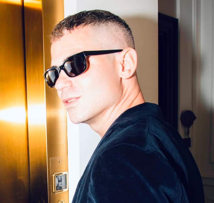 A close-up of a person standing next to a golden-hued elevator door in a modern interior space, with decorative elements visible in the background.